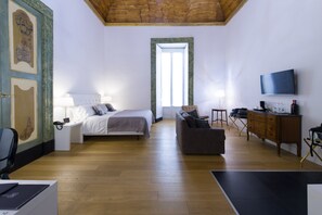 A hotel room with a bed, a sofa, a desk, a TV, and a wooden ceiling.