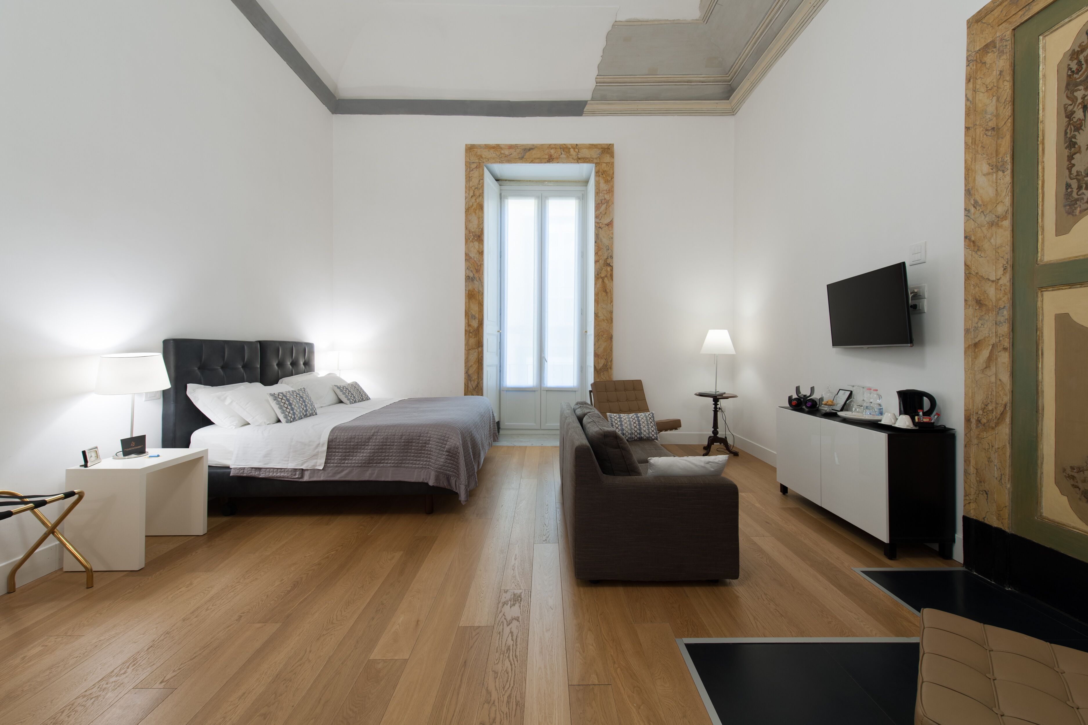 A modern hotel room with a bed, a sofa, a desk, and a TV.