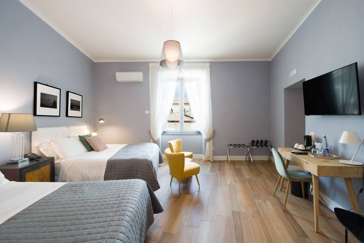 Une chambre d’hôtel moderne équipée de deux lits, d’un bureau, d’une chaise, d’une télévision et d’une fenêtre avec des rideaux.