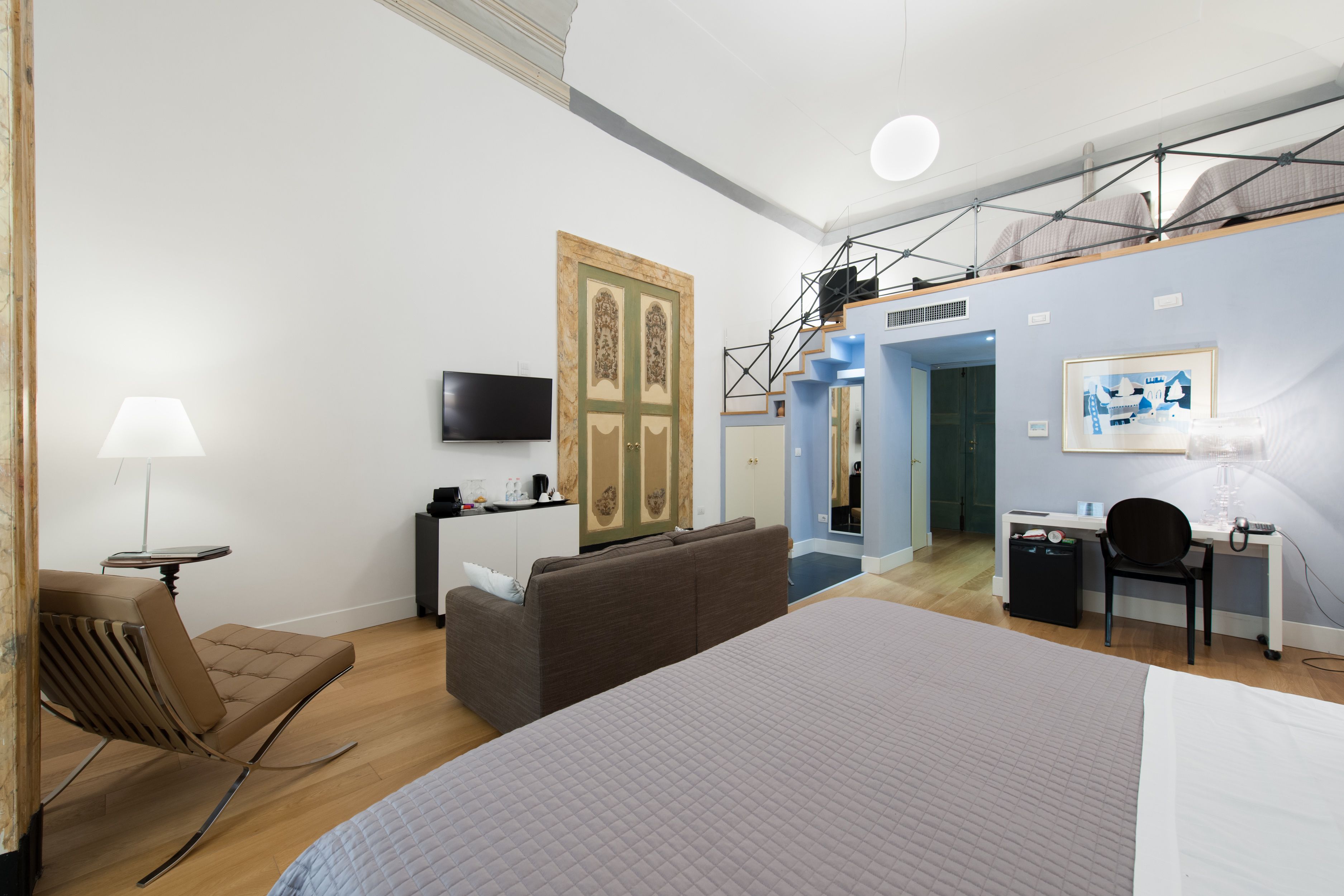 A modern hotel room with a large bed, a sofa, a desk, and a TV.