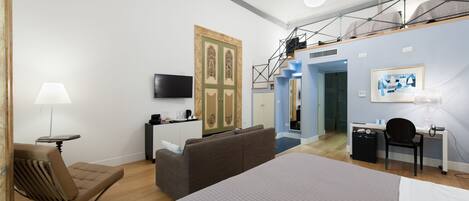 A modern hotel room with a large bed, a sofa, a desk, and a TV.