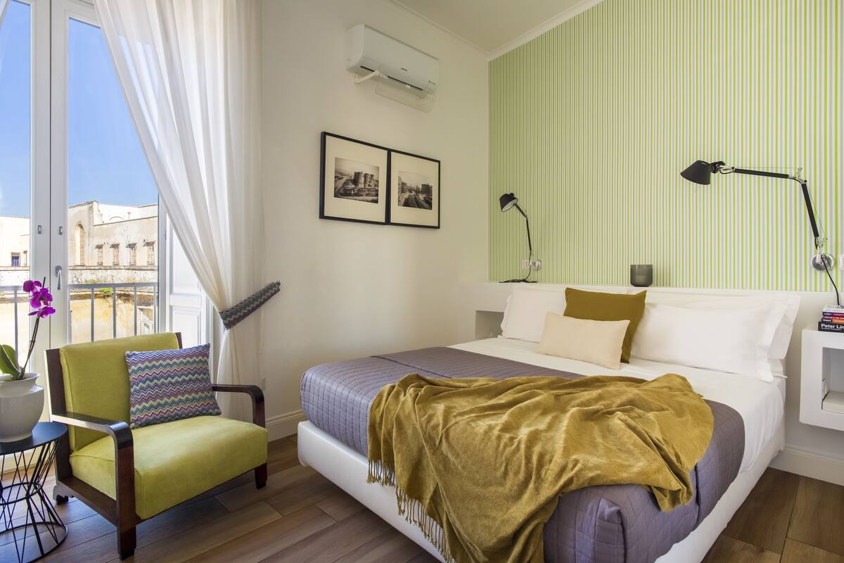 Une chambre à coucher avec un lit, une chaise, une lampe et une fenêtre avec des rideaux.