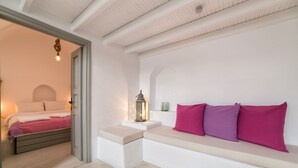 Une chambre à coucher avec un lit, un banc agrémenté de coussins, une table de chevet avec une lanterne et une porte donnant sur une autre pièce.