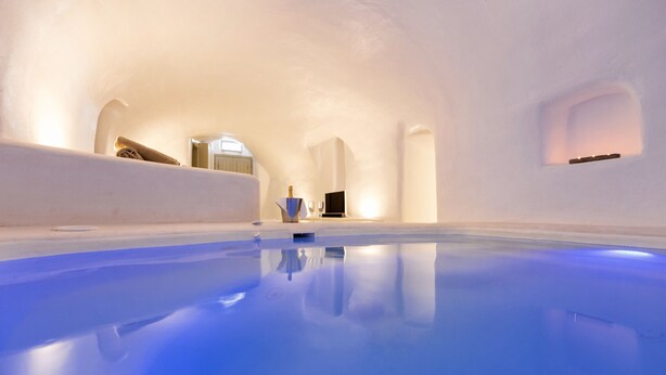 Un intérieur moderne et minimaliste avec une piscine aux carreaux bleus, des murs blancs et un coin salon accueillant agrémenté d’une bouteille et de verres.