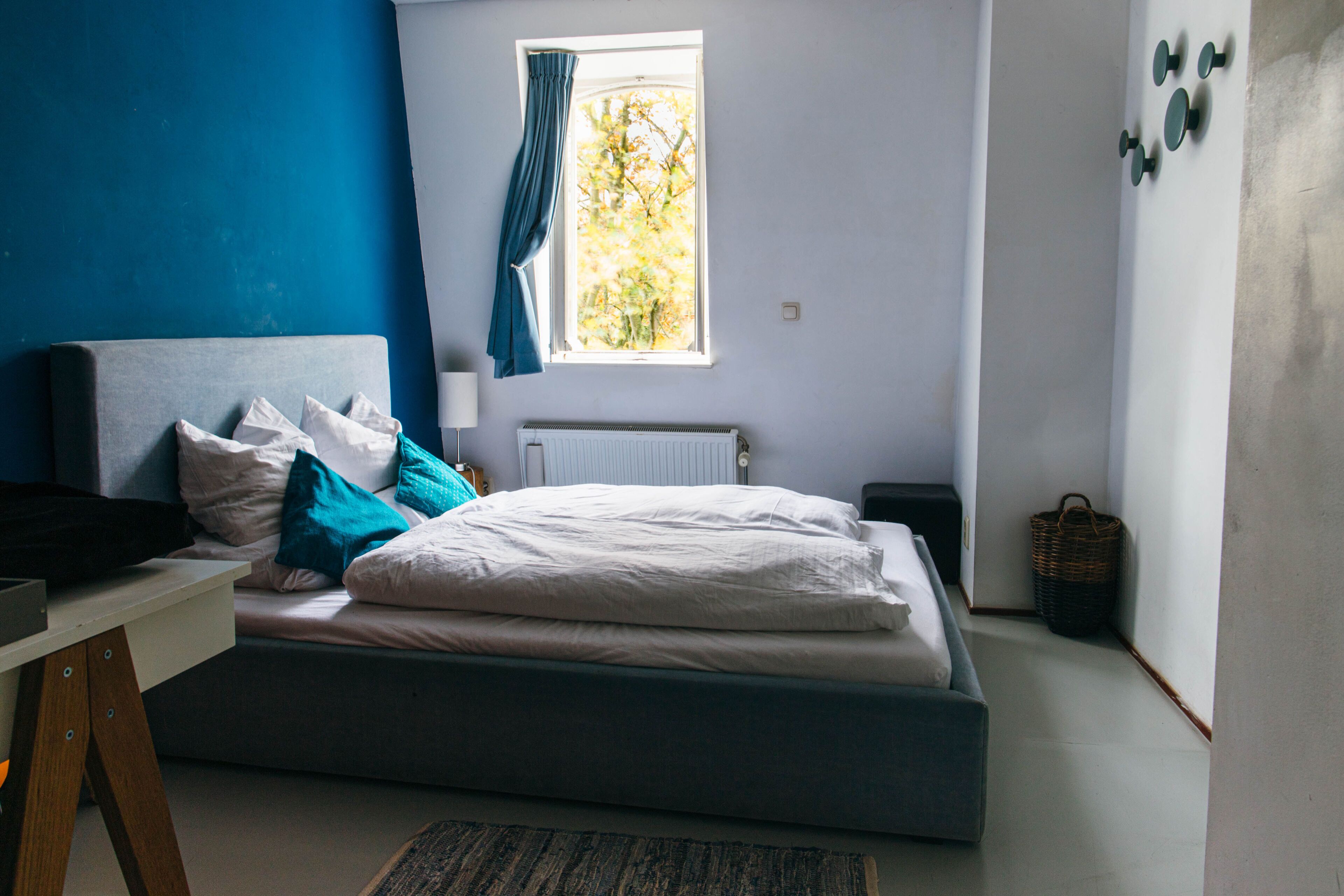 Une chambre à coucher comprenant un lit, un bureau, une fenêtre avec des rideaux, un radiateur et un chauffage fixé au mur.