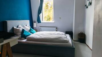 Une chambre à coucher comprenant un lit, un bureau, une fenêtre avec des rideaux, un radiateur et un chauffage fixé au mur.