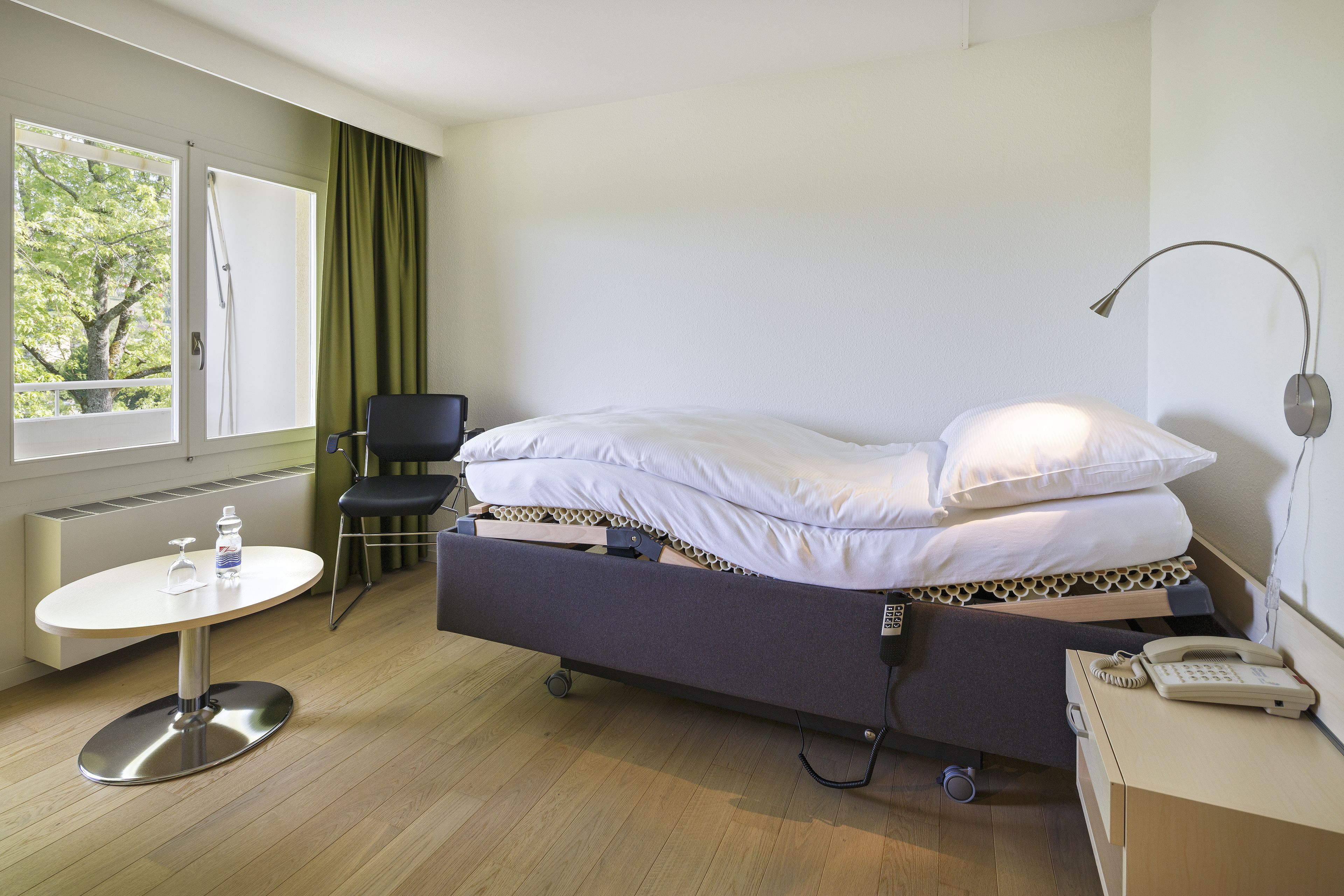 Een hotelkamer met een bed, nachtkastje, stoel en raam met gordijnen.