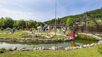 Surrounded by lush greenery, a serene pond and wooden structure invite relaxation.