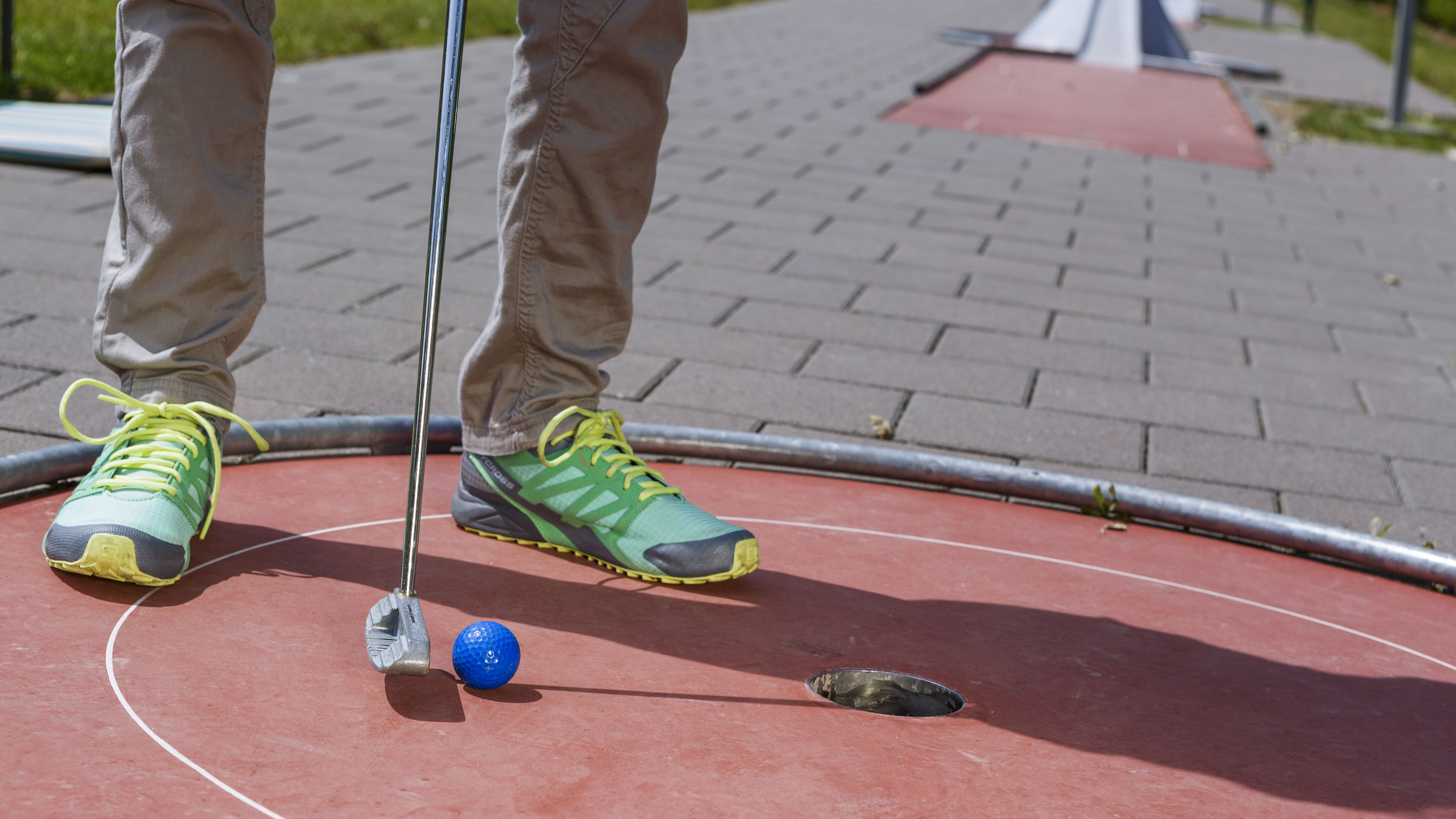 Una persona jugando golf en una cancha roja con una pelota azul y un putter.