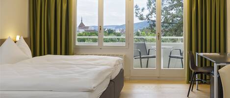 A hotel room with a bed, a desk, and a balcony with chairs.