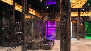 A modern bathroom with marble walls, a glass-enclosed shower area, and a purple-lit vanity. - VitalBoutique Hotel Zurzacherhof (Bad Zurzach)