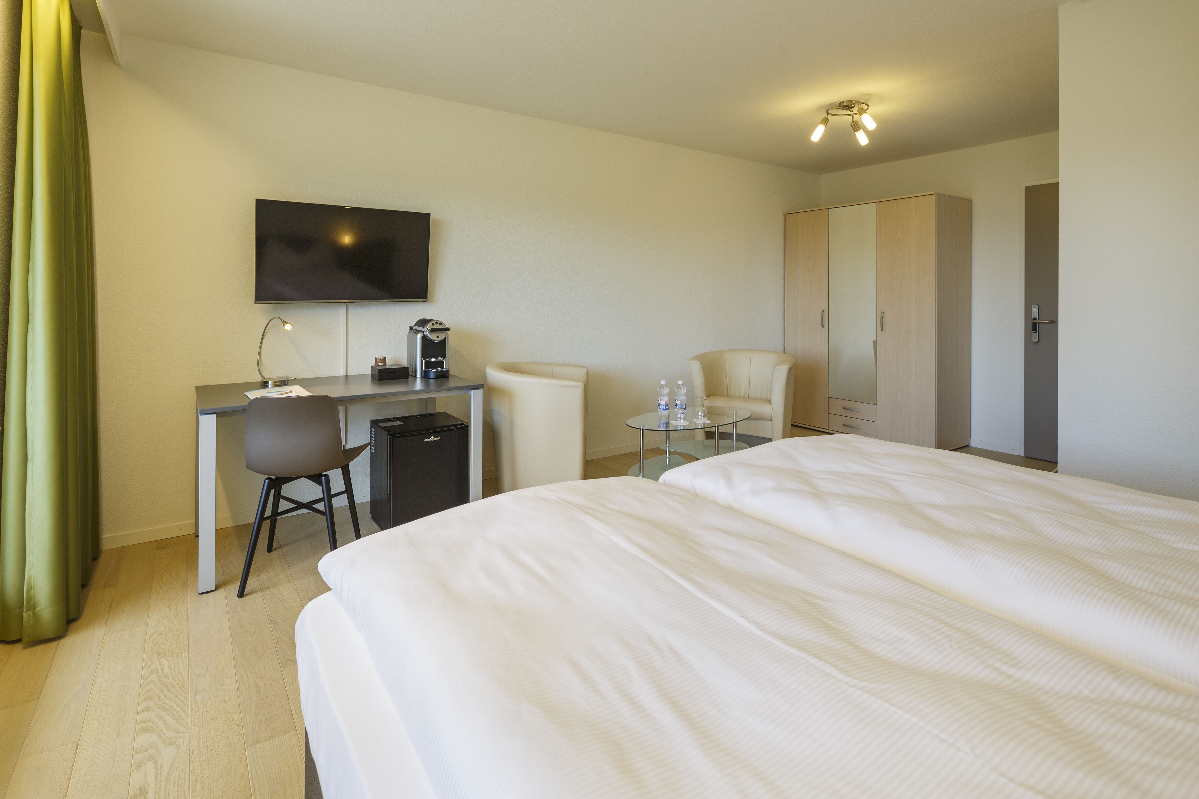 A hotel room with a bed, a desk with a chair, a television, and a wardrobe.