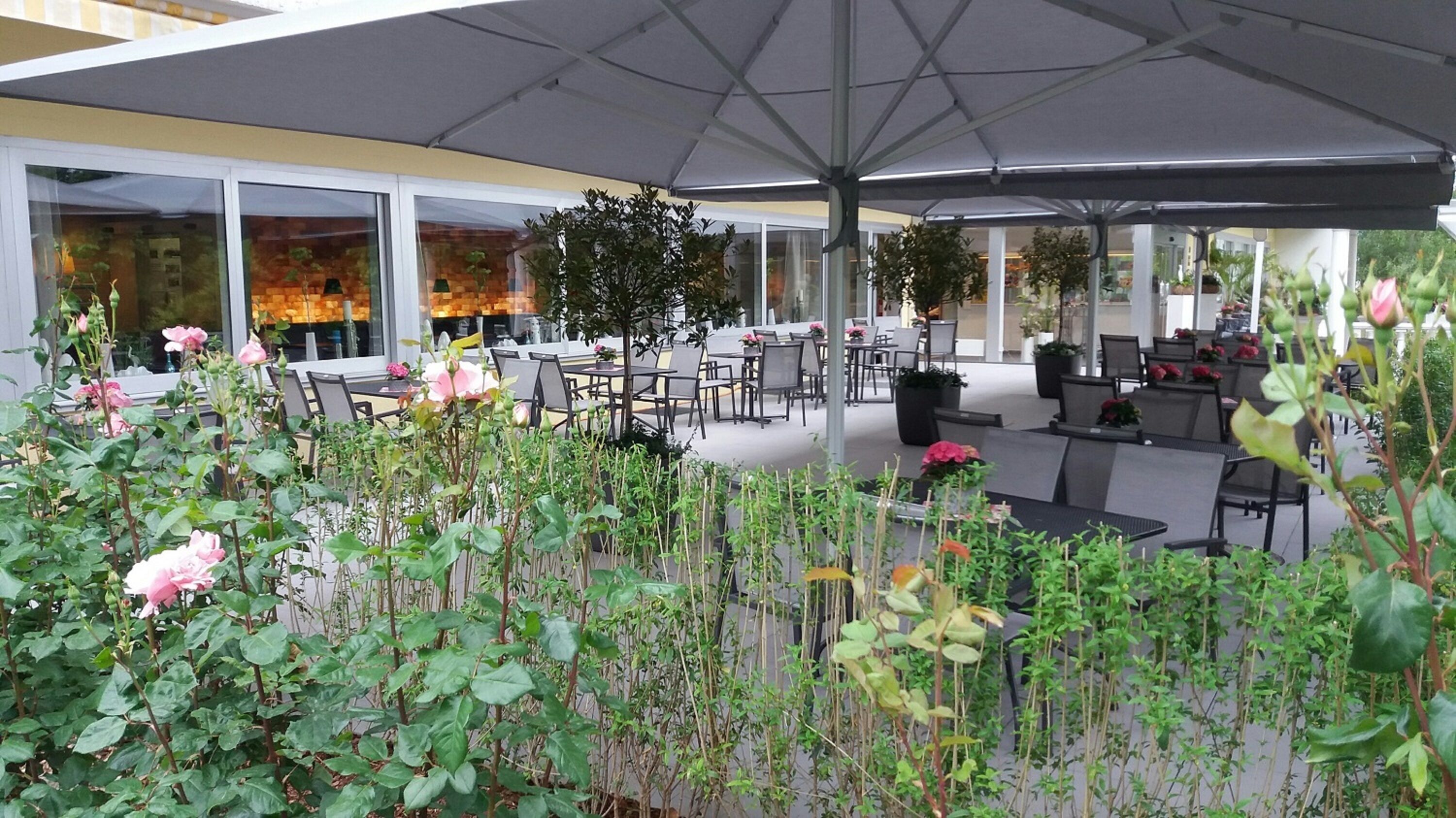 An outdoor seating area with tables and chairs, surrounded by potted plants and flowers.
