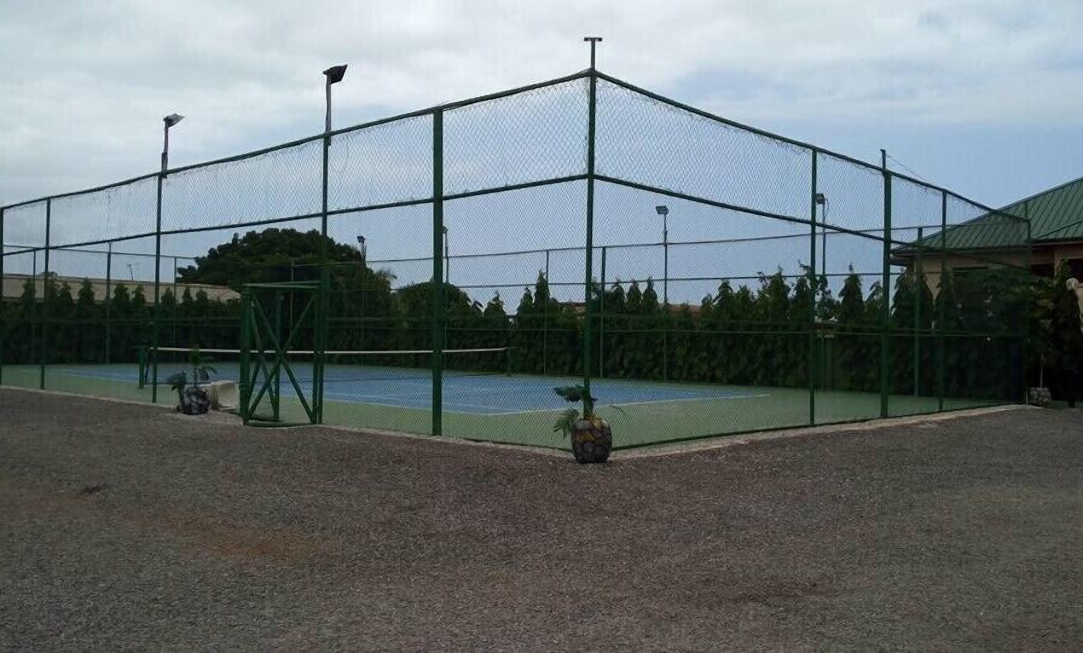 A tennis court enclosed by a chain-link fence with a gravel surface.