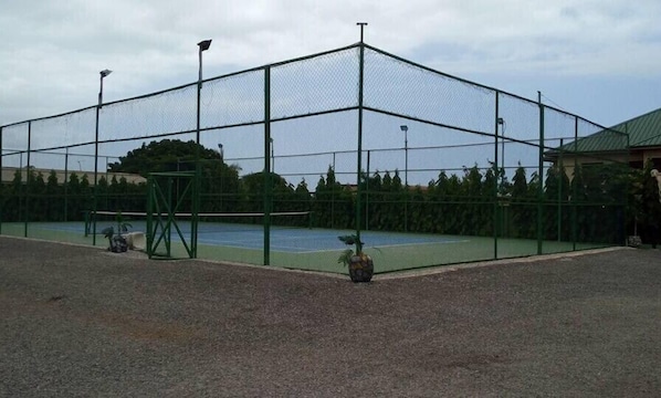 A tennis court enclosed by a chain-link fence with a gravel surface.