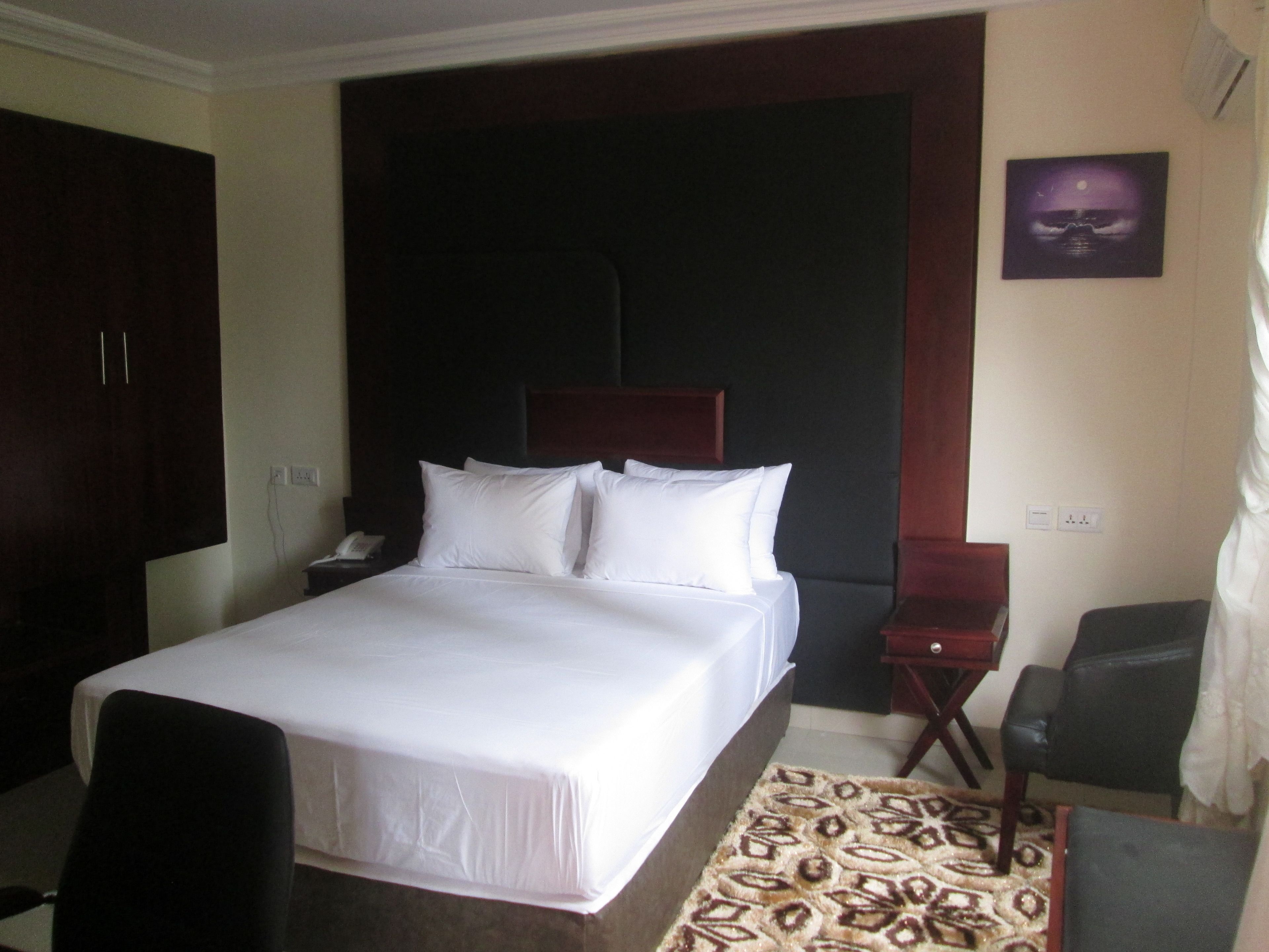 Una habitación de hotel con una cama grande, una mesita de noche con lámpara, una silla y una alfombra estampada.