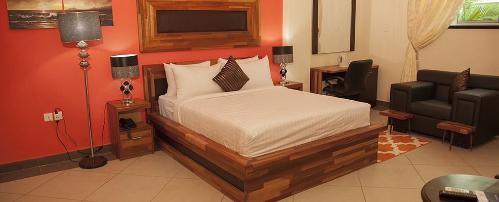 A bedroom with a wooden bed, bedside tables, a desk, a chair, and a lamp.