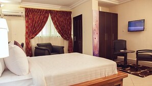 A hotel room with a bed, a desk, a chair, a wardrobe, and a TV. - Kingstel Hotel (Sekondi-Takoradi)