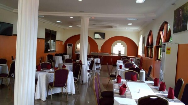 A dining area with tables set for multiple people, white tablecloths, and red napkins. - Kingstel Hotel (Sekondi-Takoradi)