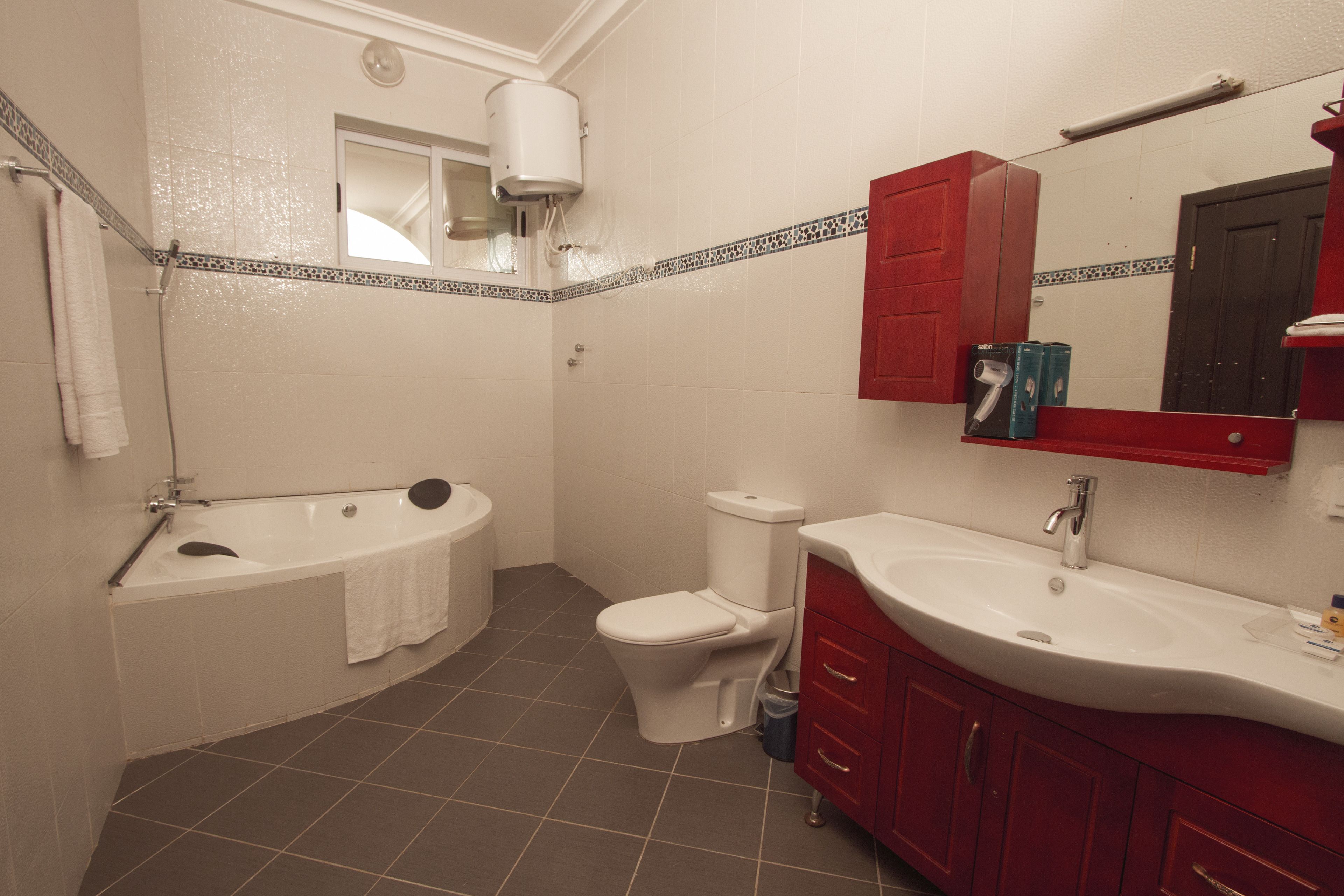A bathroom with a bathtub, toilet, sink, and red cabinets.