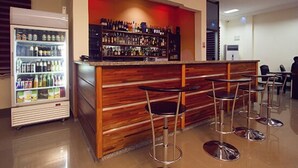 A bar area with a wooden counter, bar stools, and a beverage dispenser. - Kingstel Hotel (Sekondi-Takoradi)