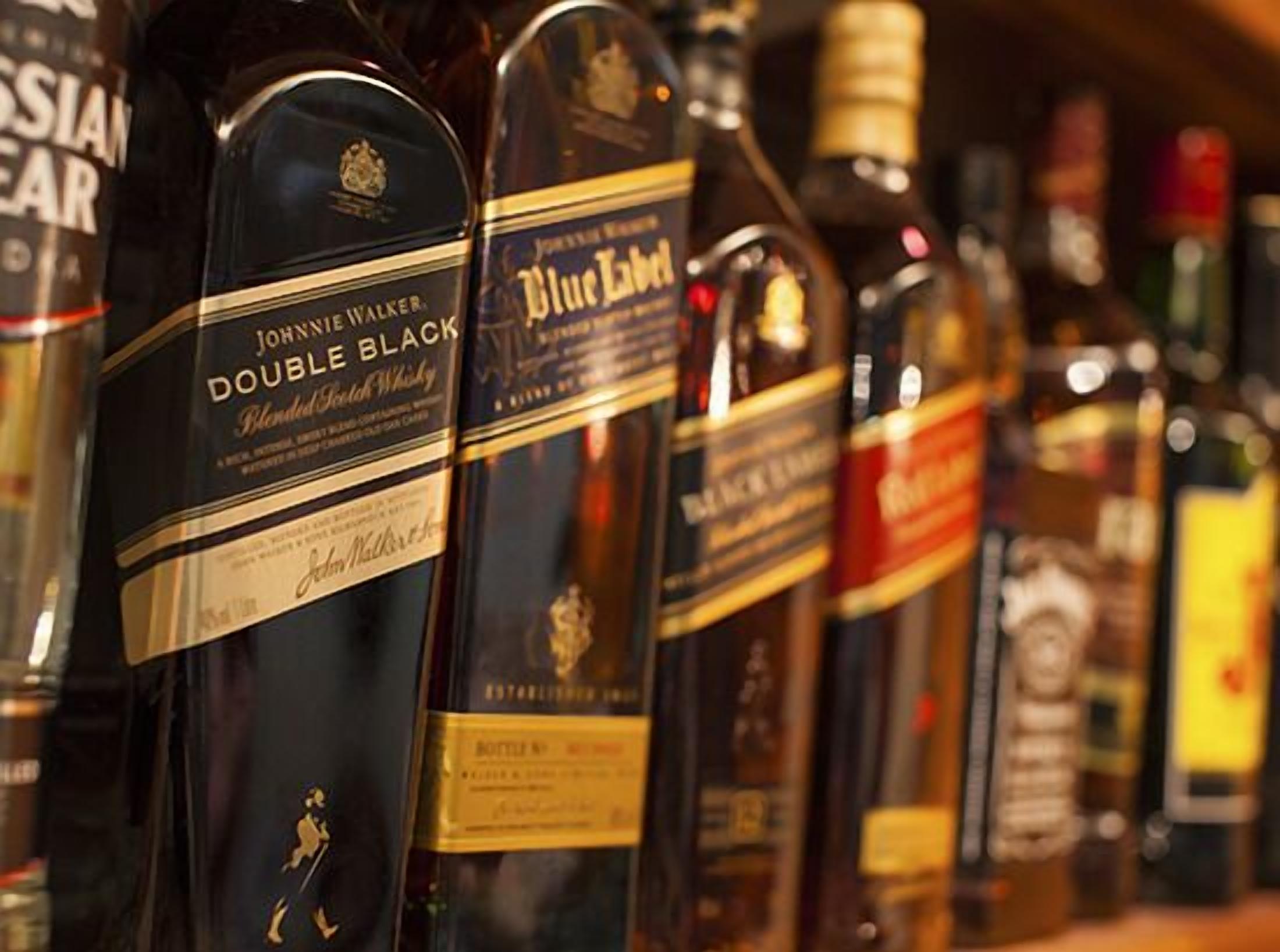Une rangée de bouteilles de whisky, dont les étiquettes sont visibles, avec des marques comme Johnnie Walker et Blue Label.