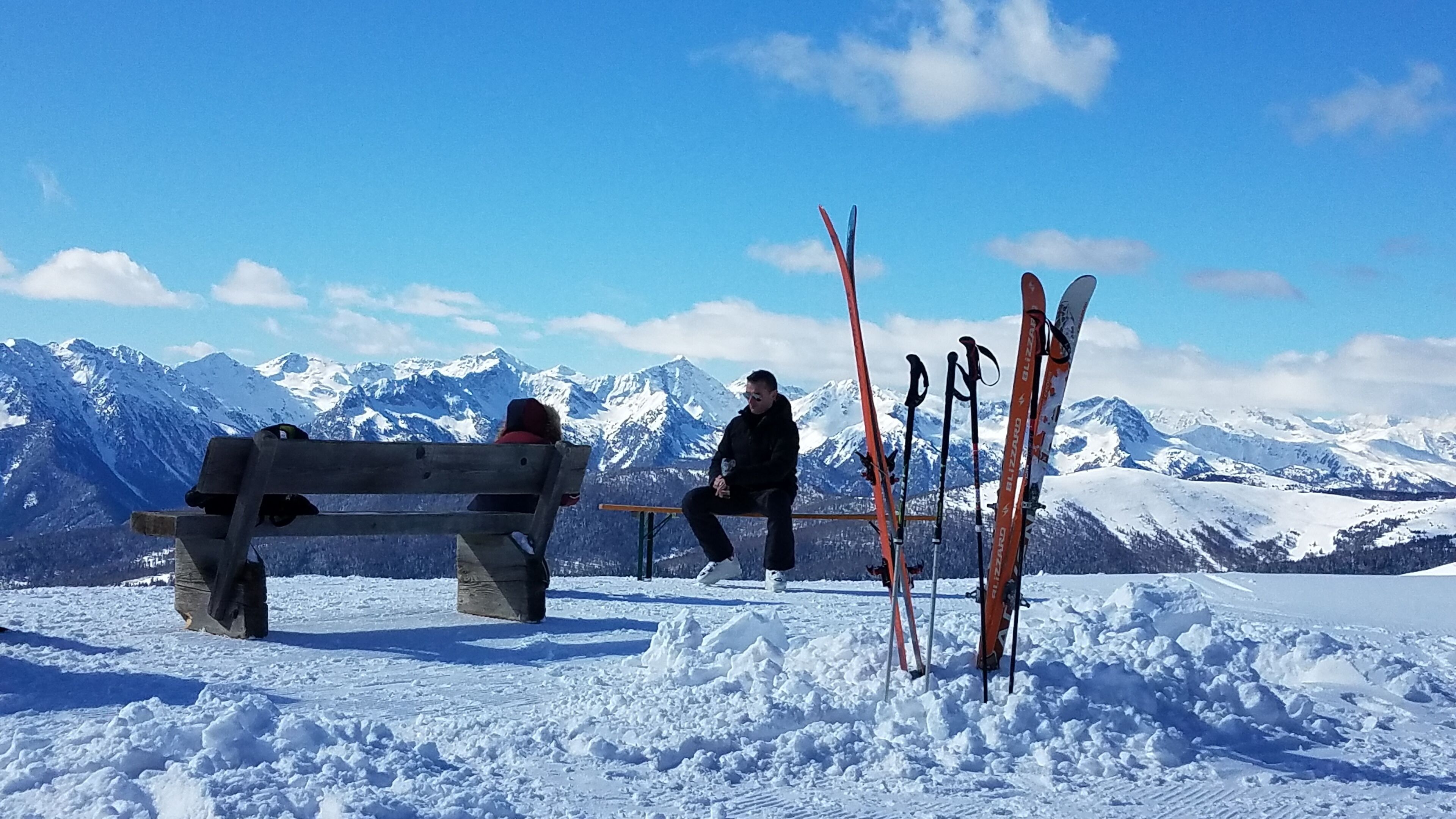 A bench and skis in a snowy landscape with mountains in the background.
