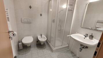 A modern bathroom with a shower, toilet, bidet, and sink.