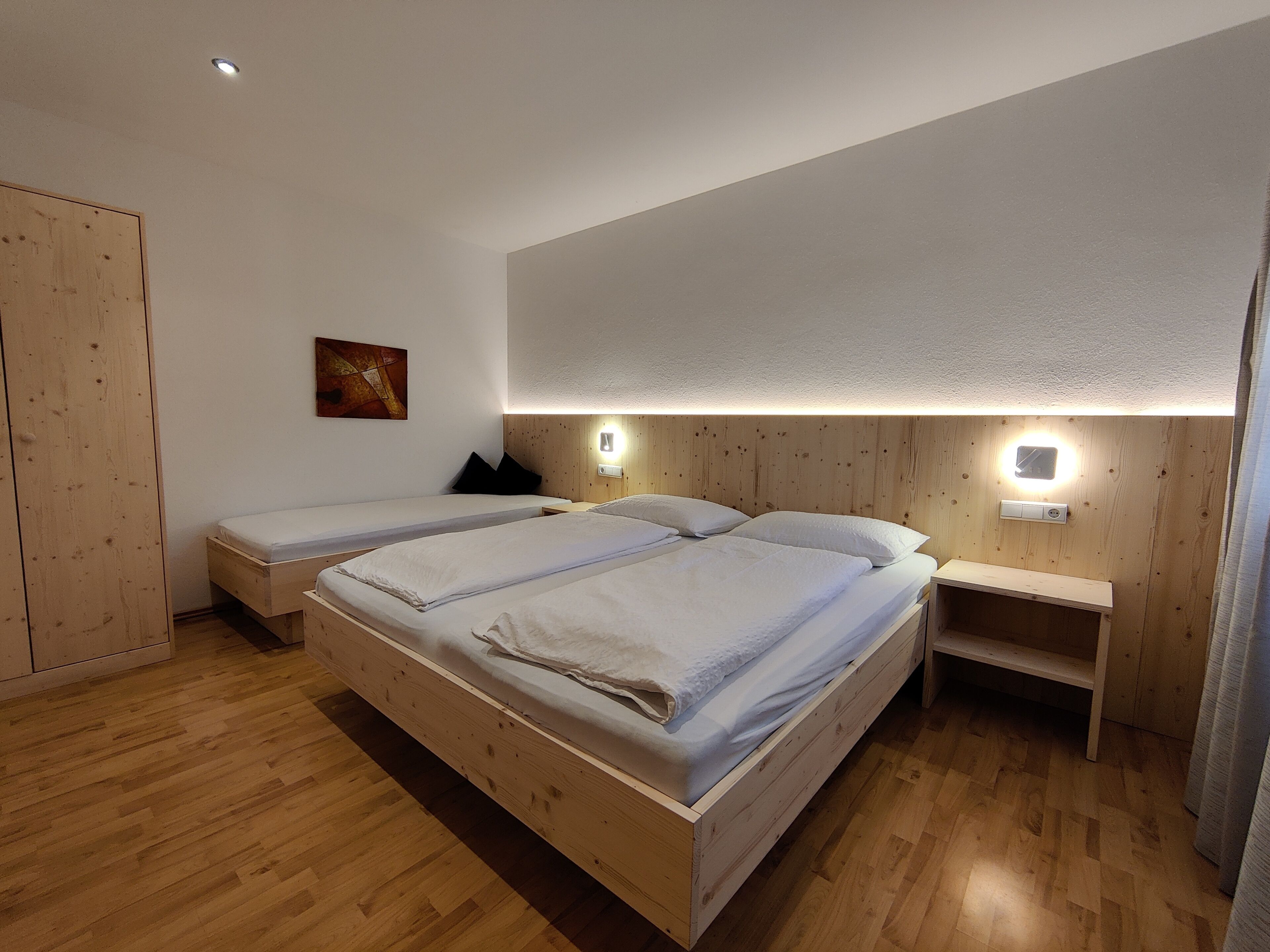 Un dormitorio moderno con dos camas de madera, una mesita de noche y una lámpara fijada a la pared.