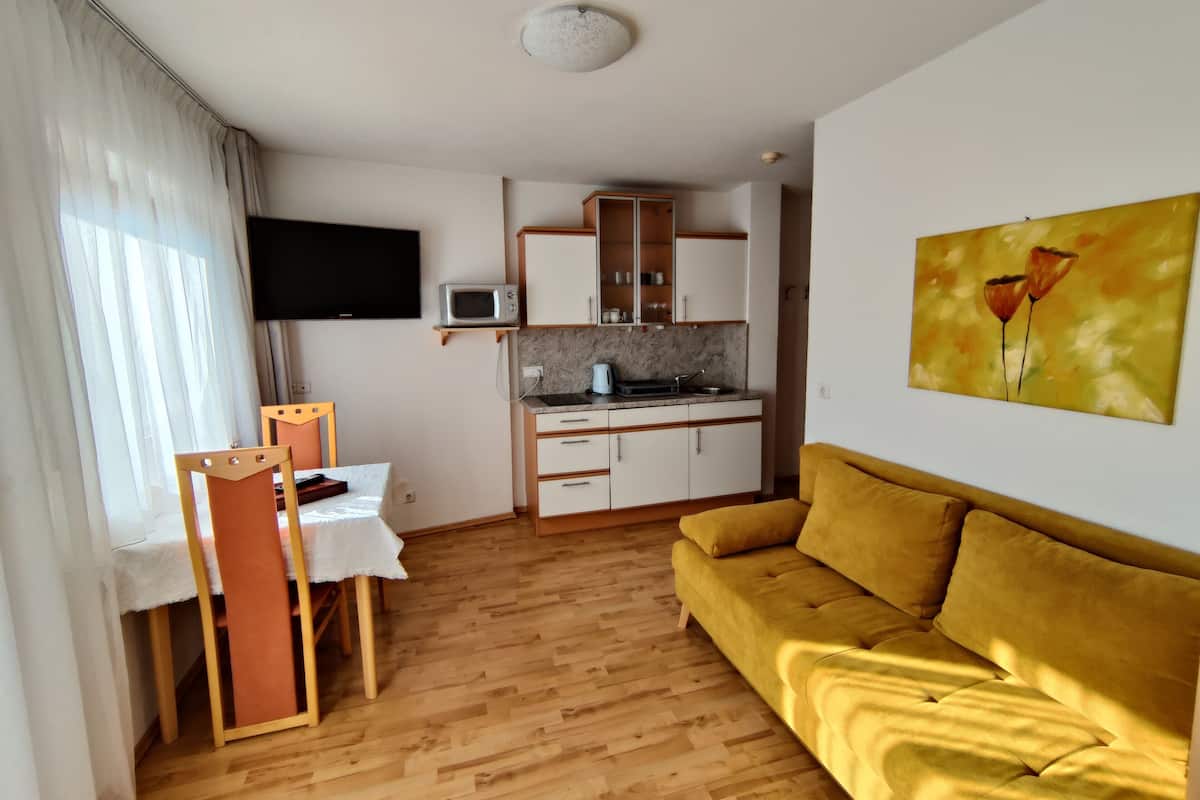 Un espacio habitable compacto con kitchenette, un sofá, una zona de comedor y un televisor montado en la pared.