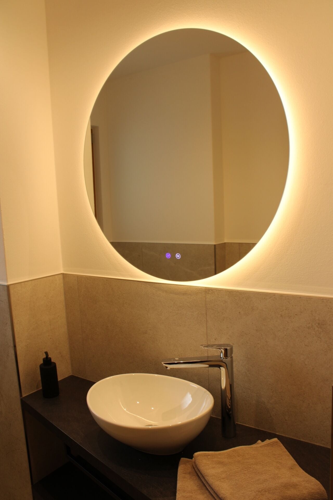 A modern bathroom with a round mirror, a white sink, and a towel on the counter.