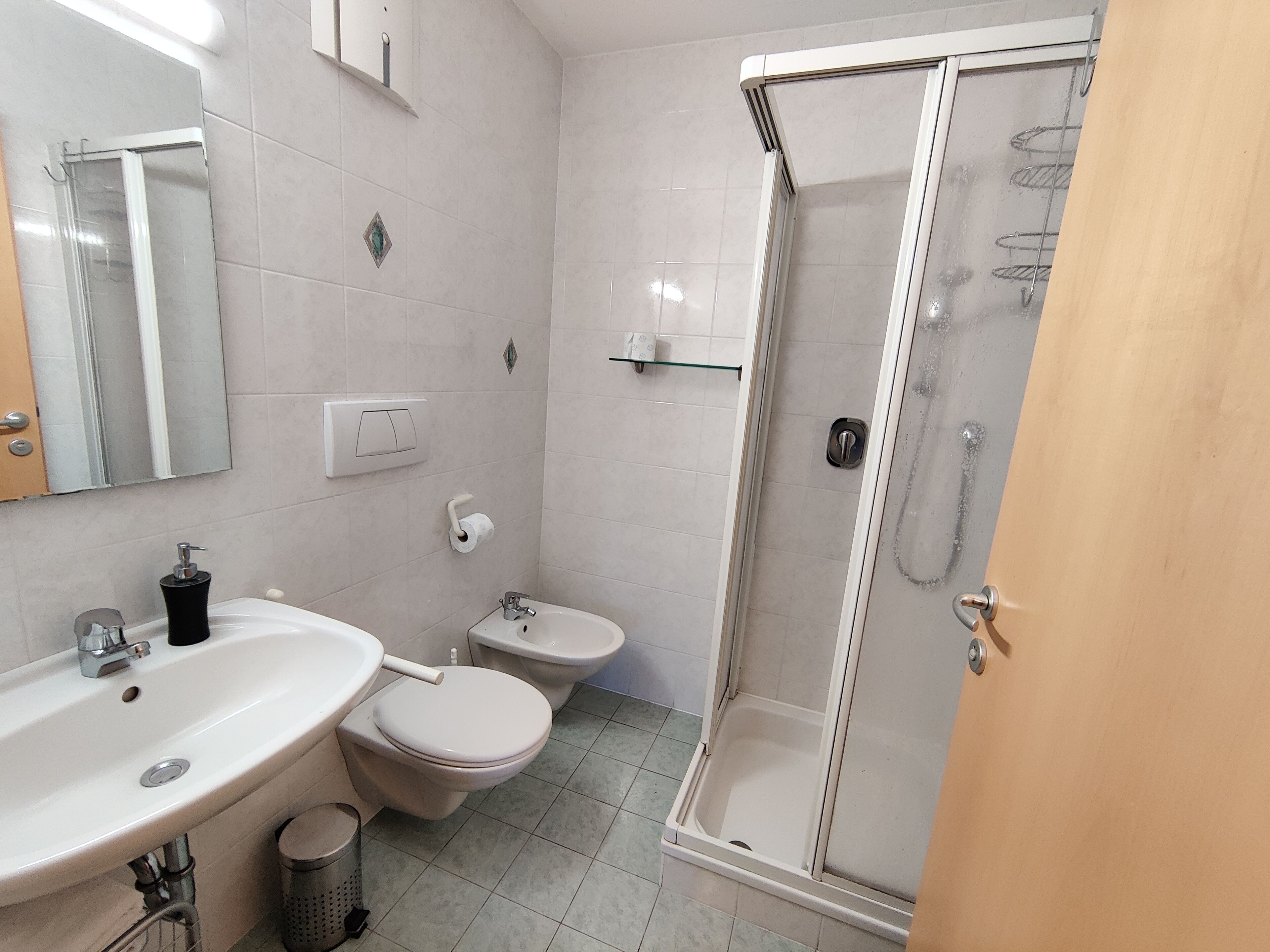 A bathroom with a sink, toilet, bidet, and a glass-enclosed shower.