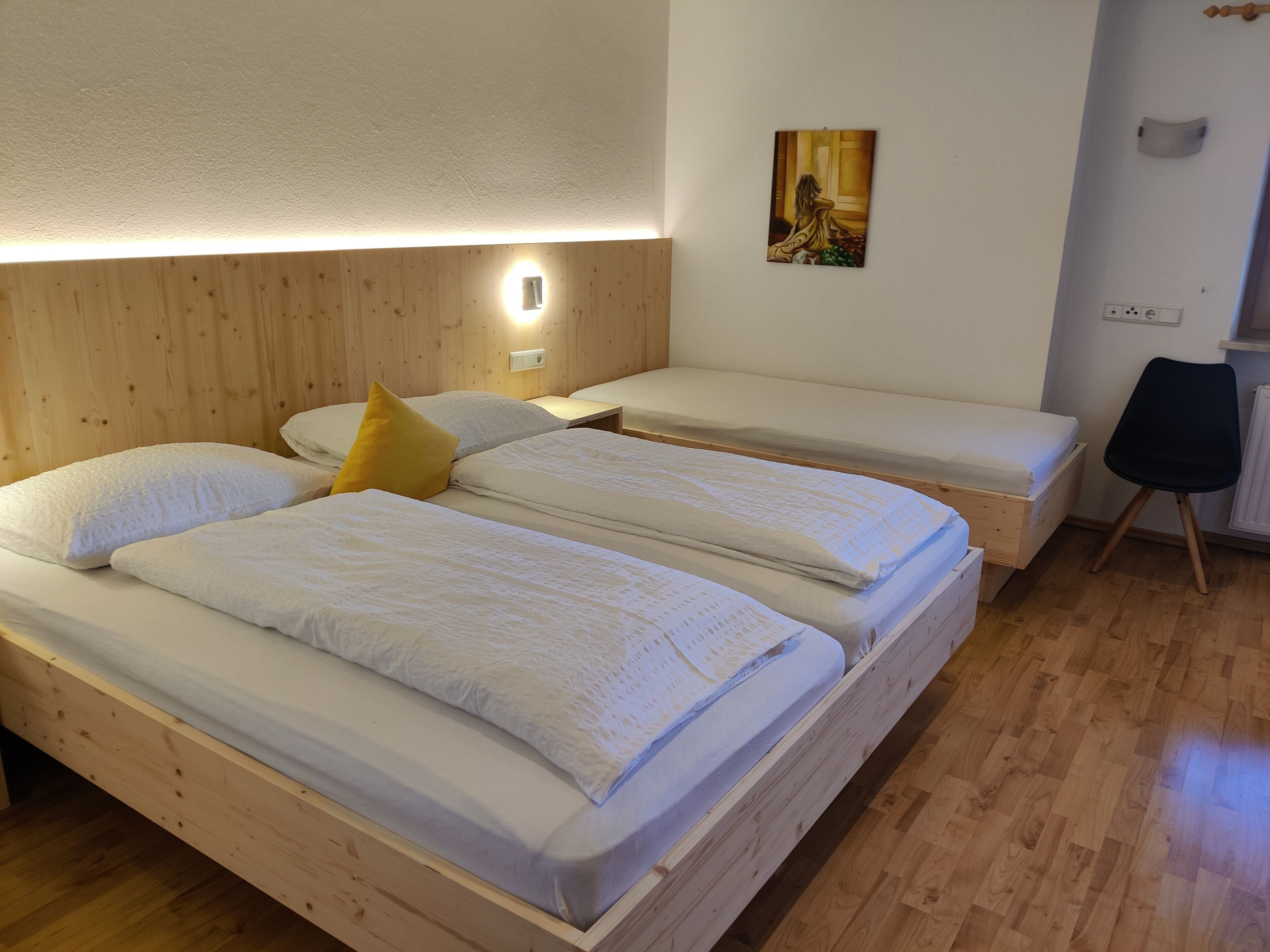 A room with two single beds, wooden headboards, a small table, and a chair.