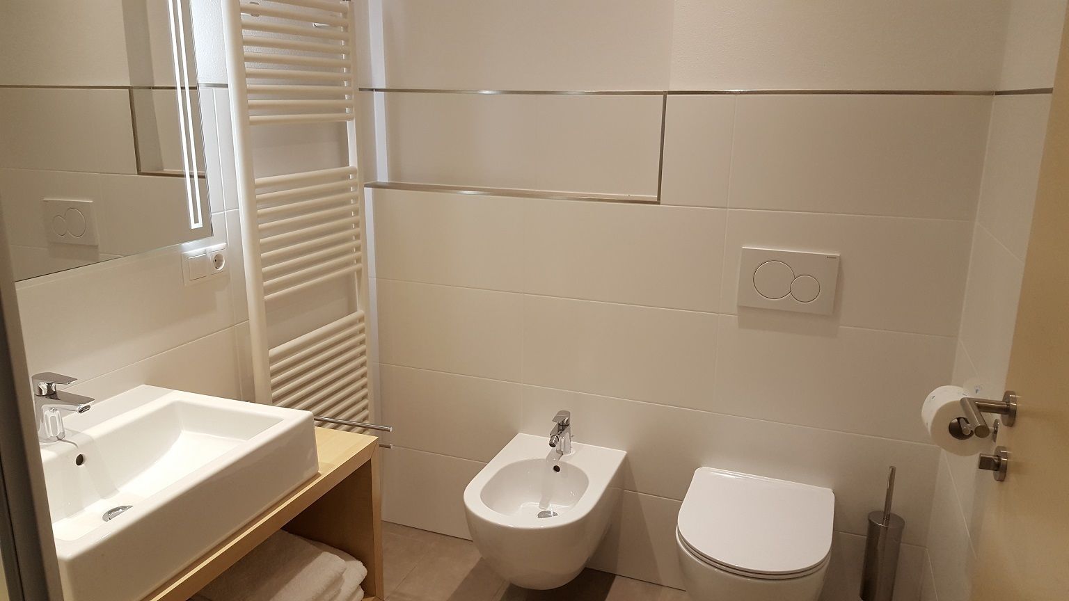 Un baño moderno con lavabo, bidé, inodoro y perchero para toallas.