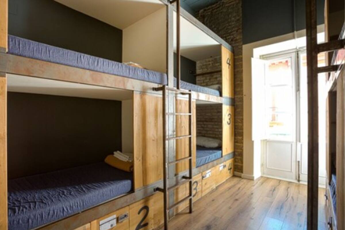 Habitación con literas, una escalera, paredes de madera y una puerta que da al exterior.