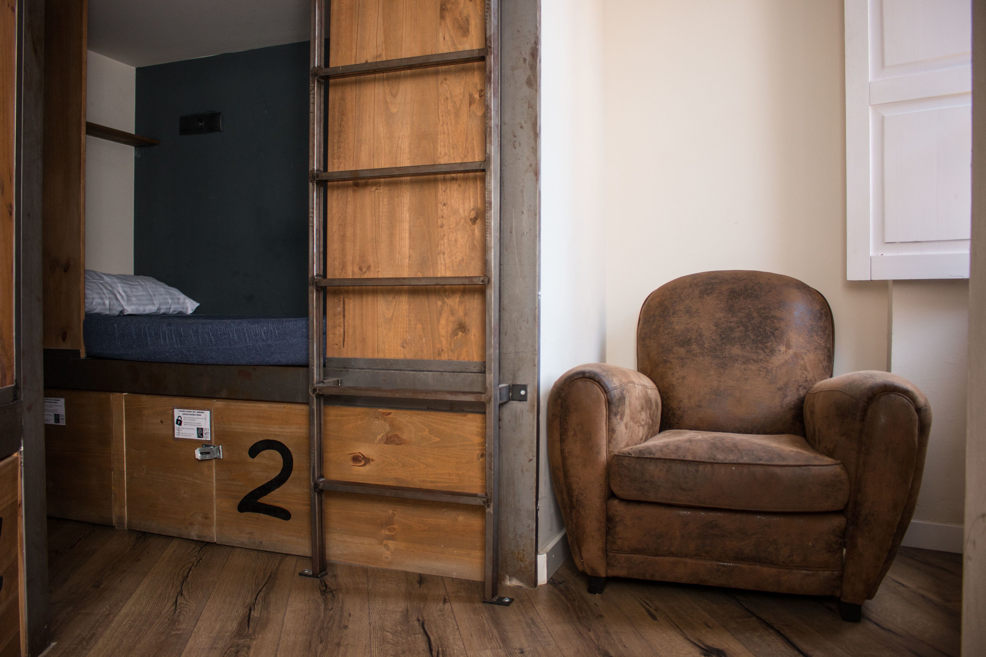 A room with a bunk bed, a wooden ladder, a brown armchair, and a white door.