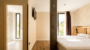 Habitación de hotel con una cama grande, cabecero de madera, televisor montado en la pared y vistas al exterior.
