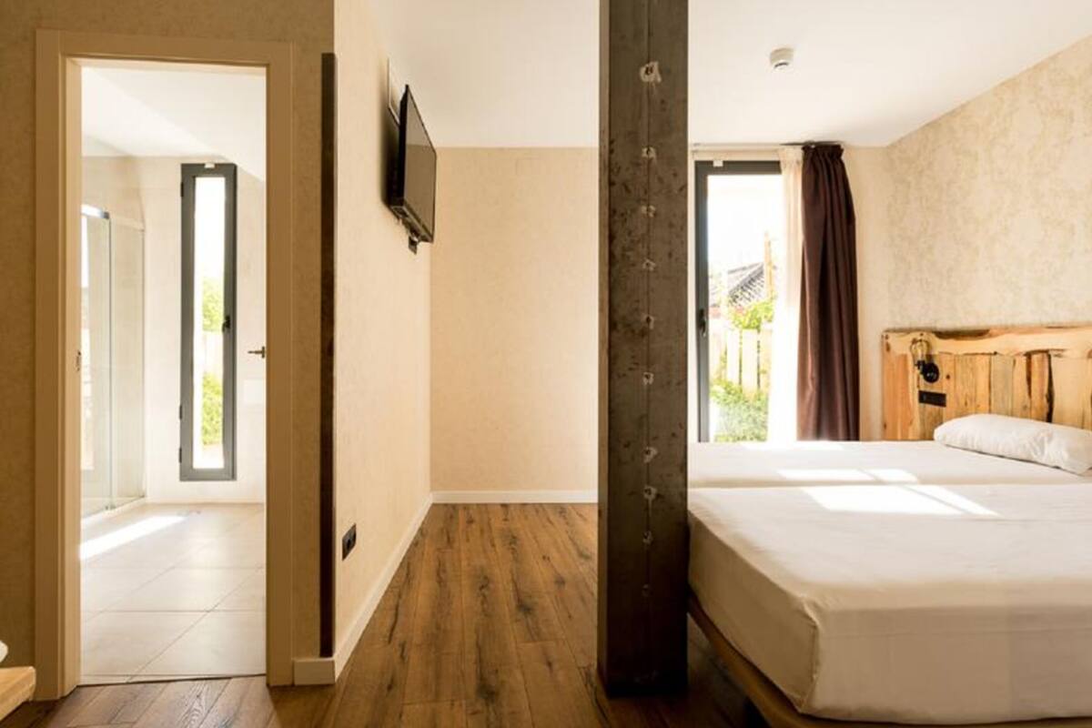 Habitación de hotel con una cama grande, cabecero de madera, televisor montado en la pared y vistas al exterior.