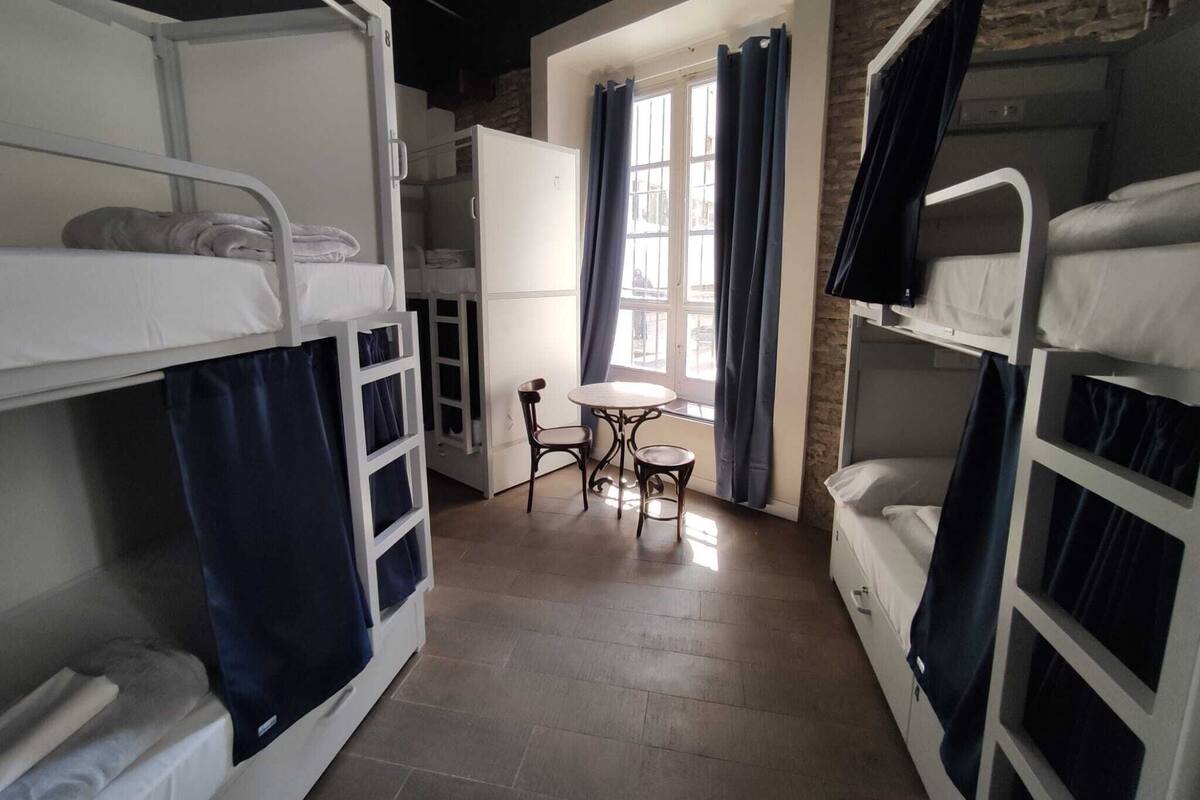 Un dormitorio con literas, una mesita pequeña y una ventana con cortinas.