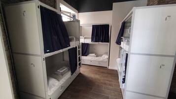 A dormitory room with bunk beds, a refrigerator, and a brick wall.