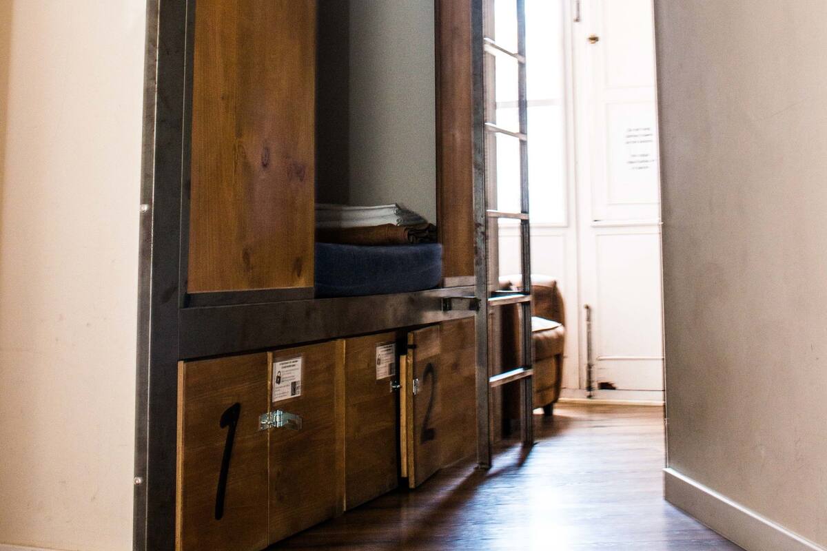 Un pasillo con armarios de madera con números, un banco y una puerta que da a otra habitación.