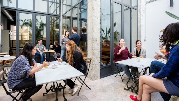 Un café al aire libre con mesas y sillas, amplias ventanas y un estilo arquitectónico moderno.
