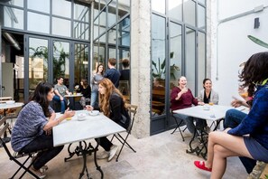 An outdoor café with tables and chairs, large windows, and a modern architectural style. - Black Swan Hostel Sevilla (Seville)