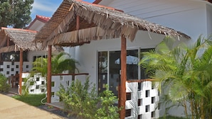 Un resort con estructuras de techo de paja, palmeras y un edificio blanco con grandes ventanales.