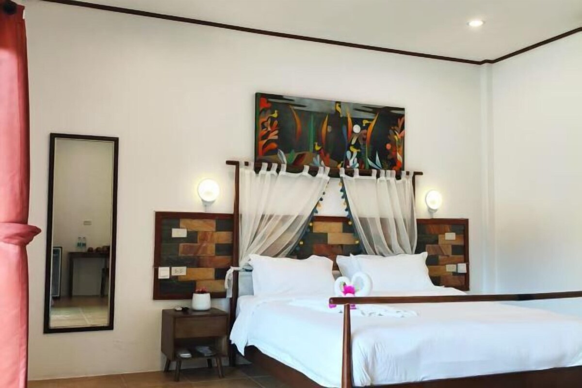 A hotel room with a bed, a nightstand, a mirror, and a wall-mounted artwork.
