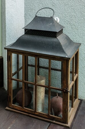 A lantern with a metal top and glass panels, placed on a wooden surface against a textured wall. - All In Apartments (Kraków)