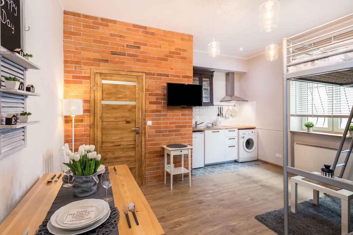 A modern kitchen with a brick wall, wooden door, and white appliances.