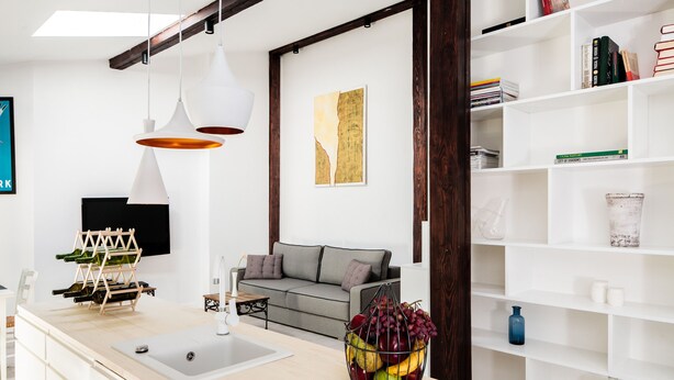 A modern living room with a kitchen island, a grey sofa, and a bookshelf. - All In Apartments (Kraków)