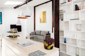 A modern living room with a kitchen island, a grey sofa, and a bookshelf.