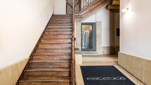 A wooden staircase with a black doormat reading "Estetica" leading to a room with a glass door and a stone wall. - All In Apartments (Kraków)
